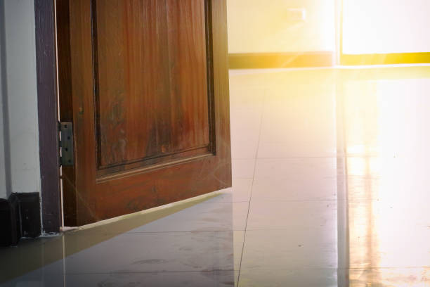 Деревянная дверь слегка приоткрыта, позволяя яркому солнечному свету струиться на кафельный пол.
