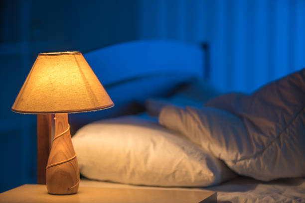 Уютная спальня с зажженной прикроватной лампой и подушками на кровати.